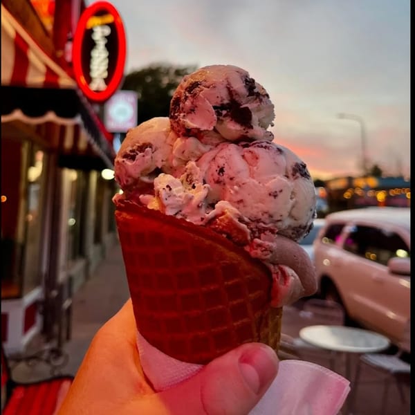 Hand holding a Grand Ole Creamery waffle cone with three scoops of cookies and cream ice cream at dusk.